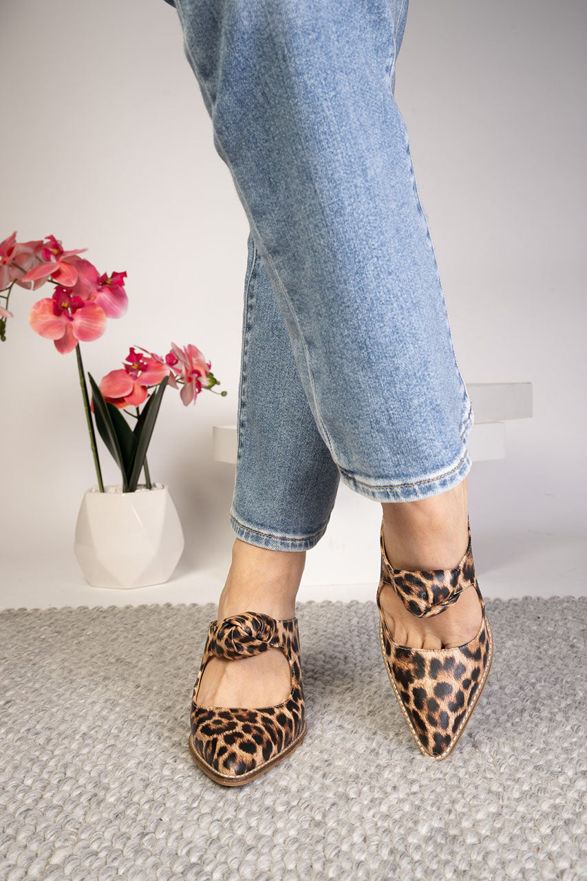 Person wearing leopard print shoes with a vase of flowers in the background