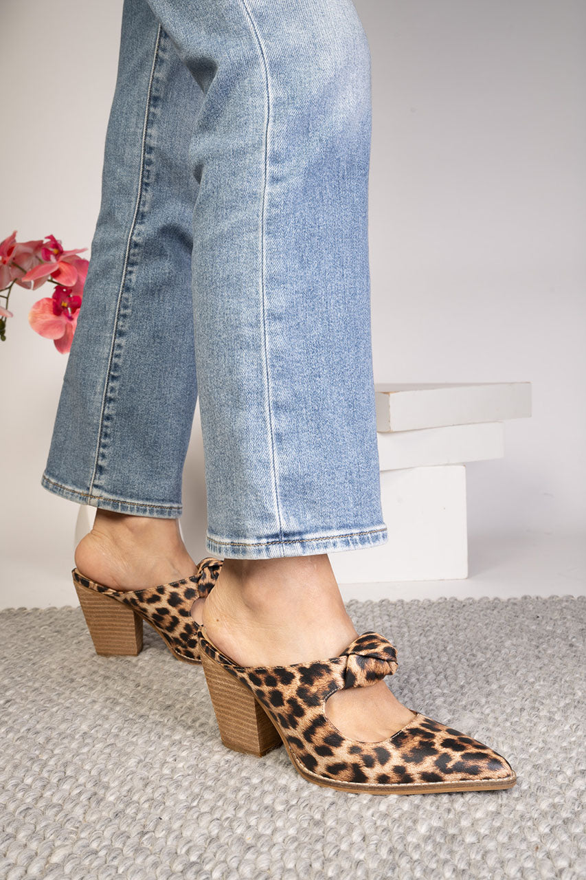 Person wearing leopard print shoes with a block heel and bow detail, paired with light blue jeans.