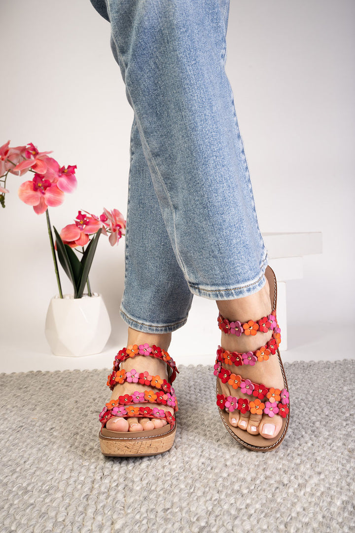 Person wearing colorful sandals with floral straps on a neutral background