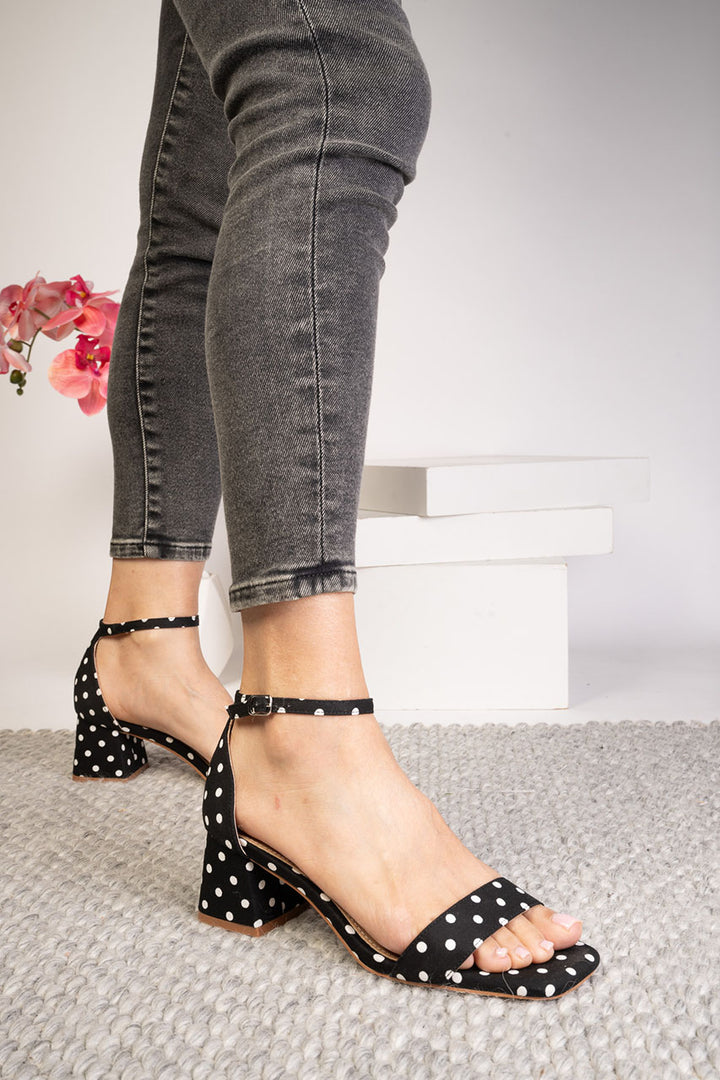 Black polka dot sandals worn with gray jeans on a light background