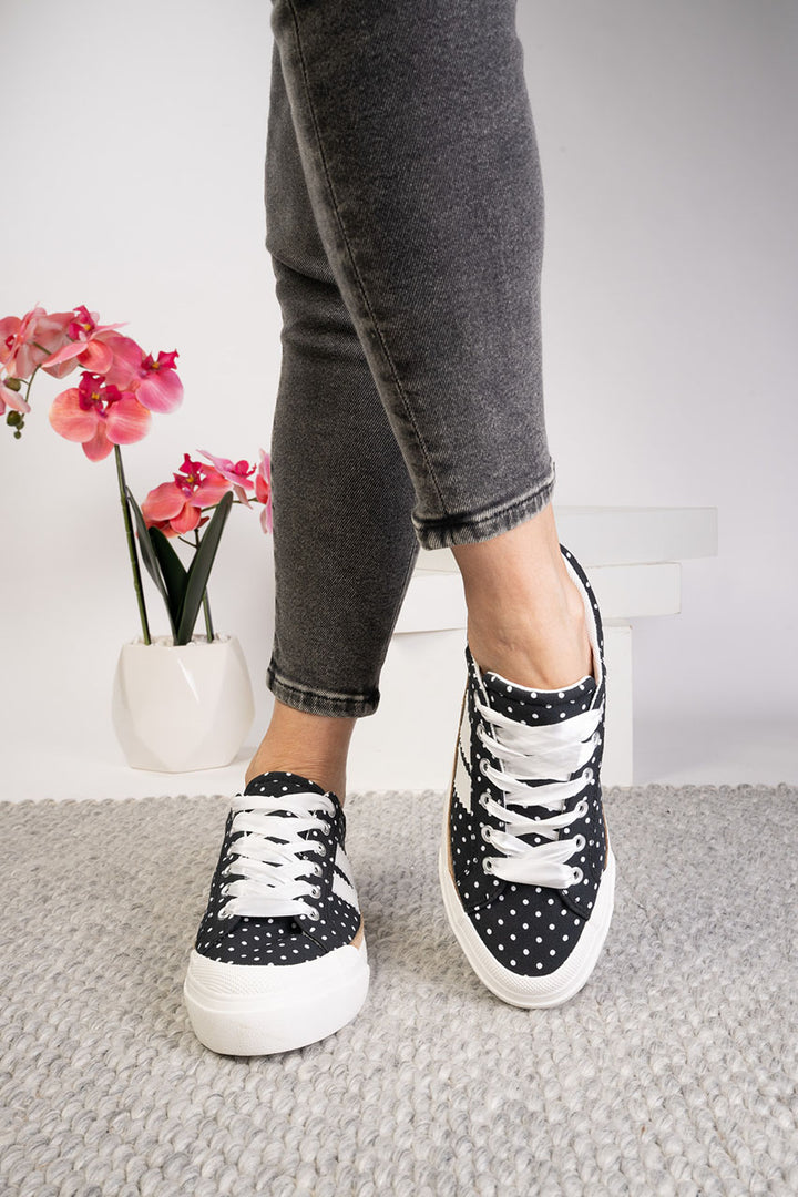 Person wearing black polka dot sneakers with white laces on a neutral background