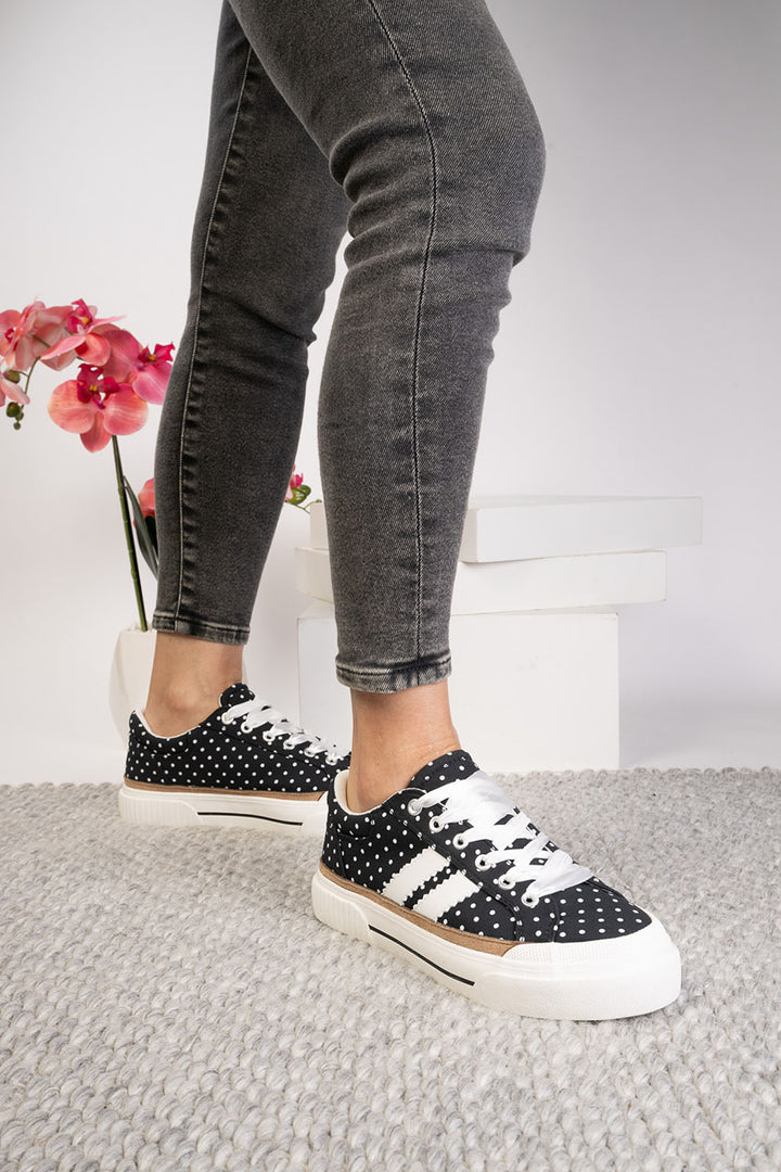 Black and white polka dot sneakers worn with gray jeans on a light background