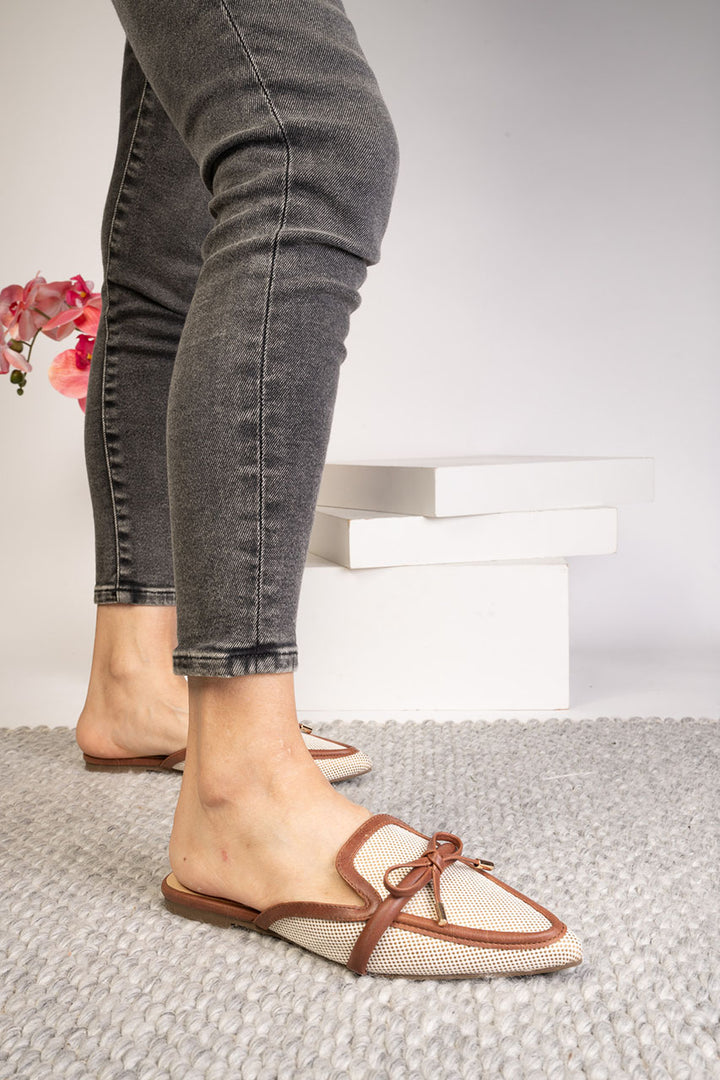 Person wearing gray jeans and white shoes with brown accents on a light background