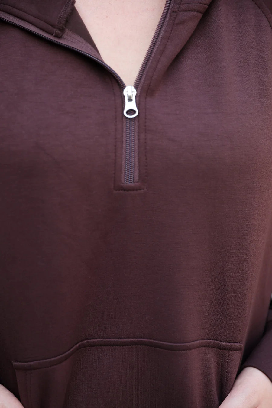 Close-up of a person wearing a chocolate quarter-zip pullover sweatshirt with a zipper pull.