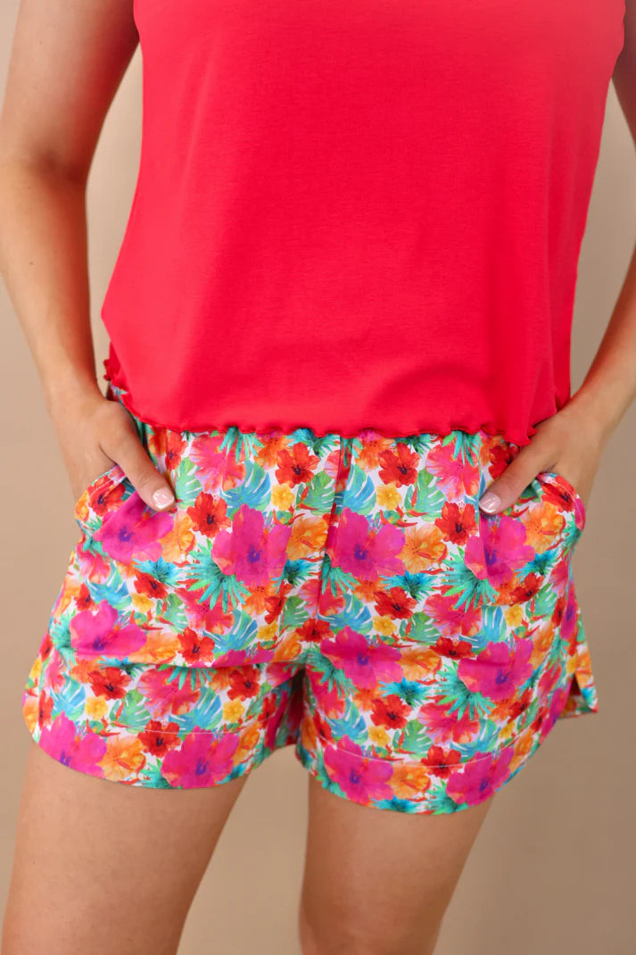 Person wearing a bright red top and colorful floral shorts on a beige background