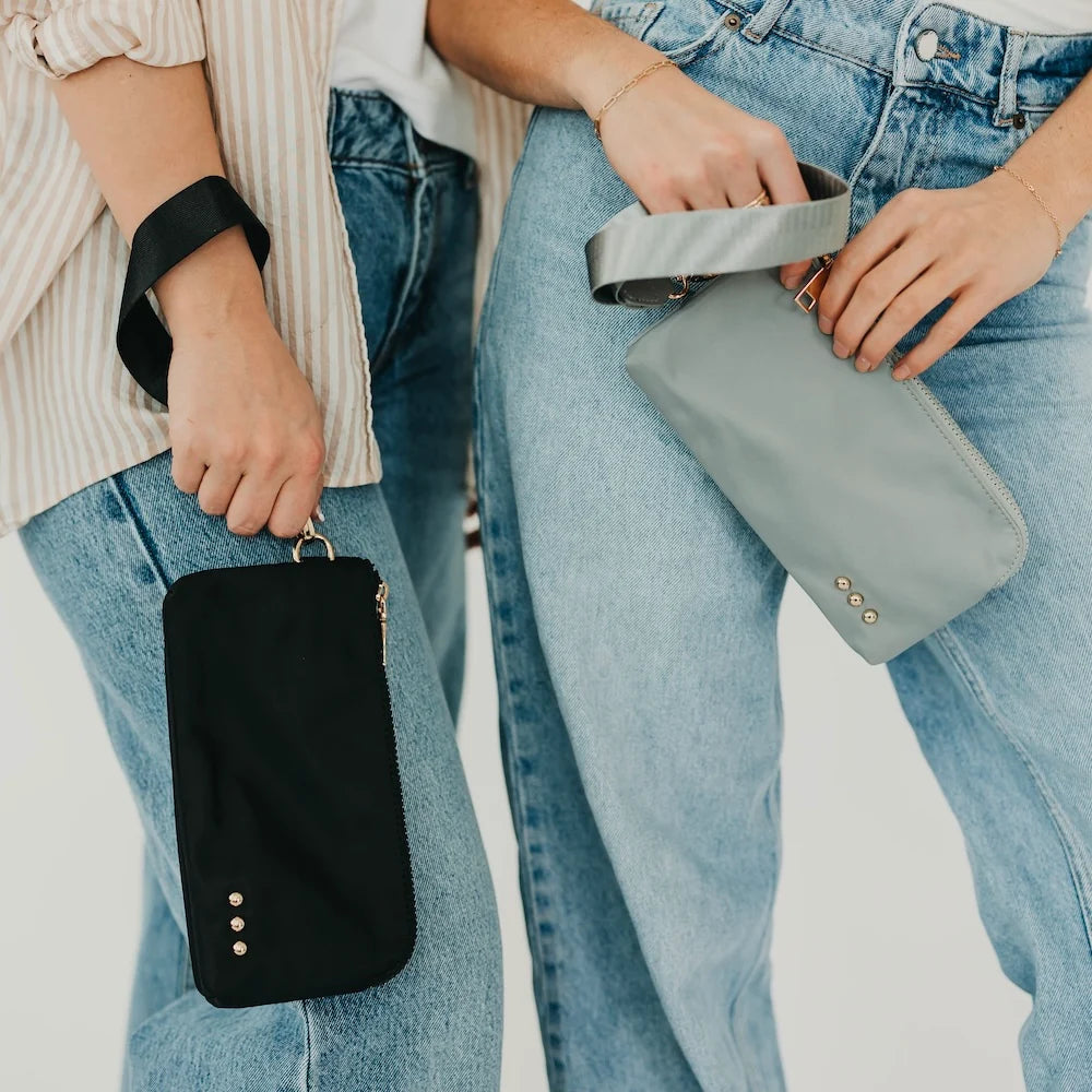 Two people holding wristlet wallets, one is black and the other is gray
