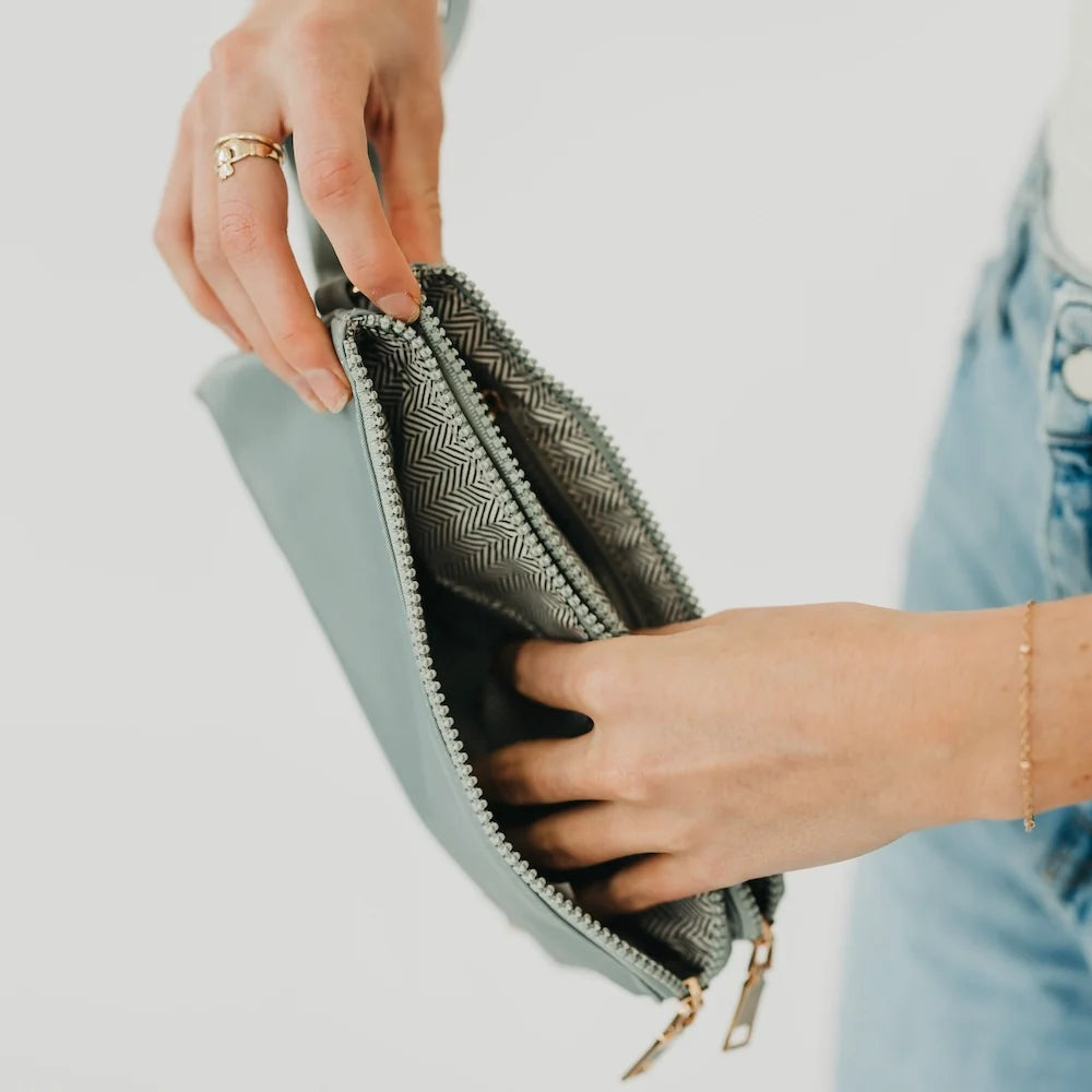 Hands holding a gray wristlet open to show compartments