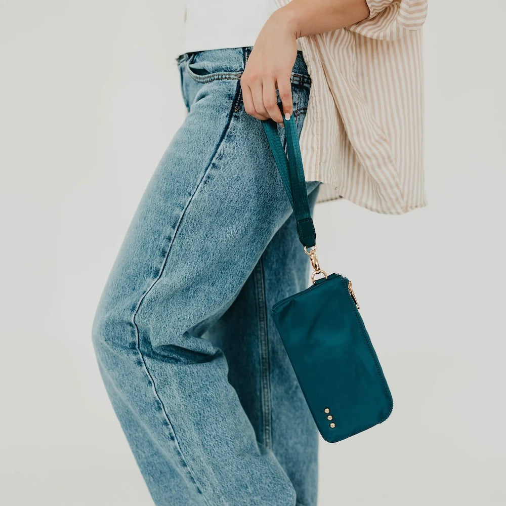 Person wearing jeans holding a teal wristlet wallet