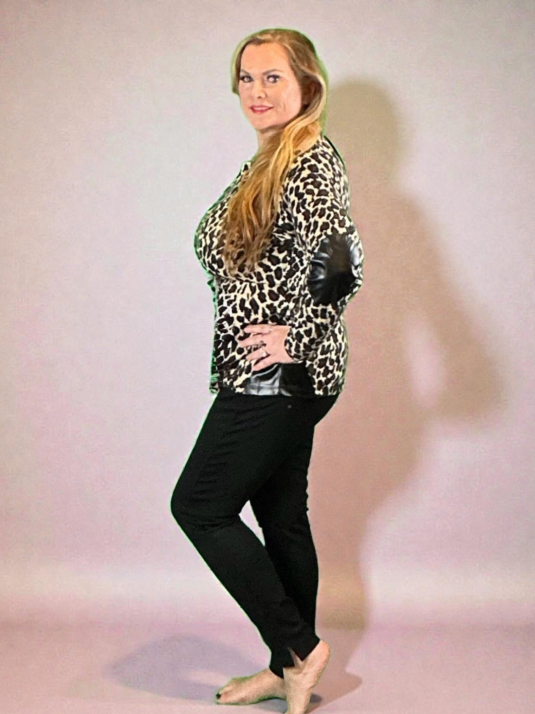 Woman wearing black pants with split at the bottom hem and animal print top against neutral background.