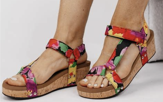 Colorful floral sandals on feet against a neutral background