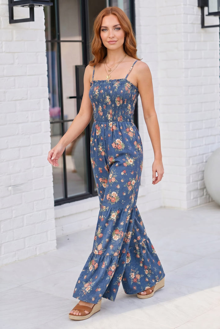 Woman wearing a blue floral dress standing against a white brick wall.