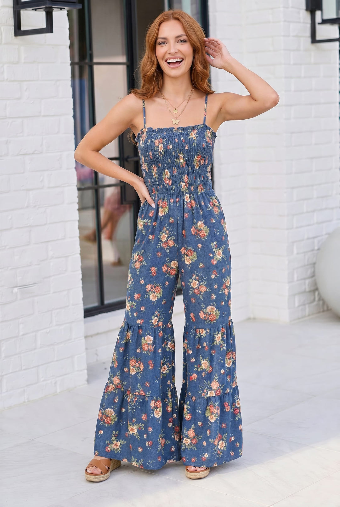Woman wearing a blue floral jumpsuit standing against a white brick wall.