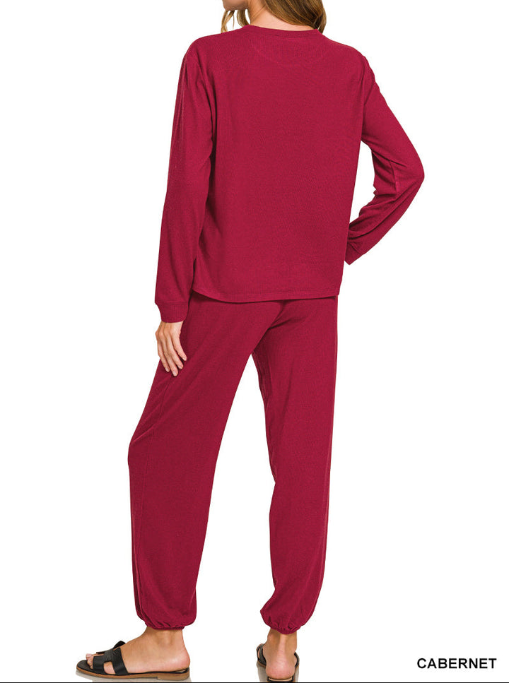 A woman modeling a matching two-piece loungewear set in a deep cabernet red color, viewed from the back. The set includes a long-sleeve top and jogger pants, shown against a plain white background with a &