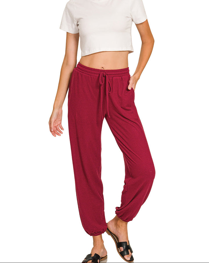 A woman modeling a white short-sleeve crop top and burgundy drawstring harem pants against a plain white background.