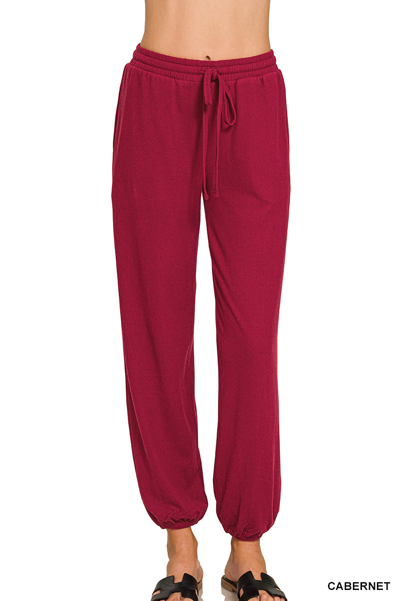 A person wearing jogger-style pants in a deep cabernet red color, shown from the waist down against a plain white background. The pants have an elastic waistband with a drawstring and elastic cuffs at the ankles.