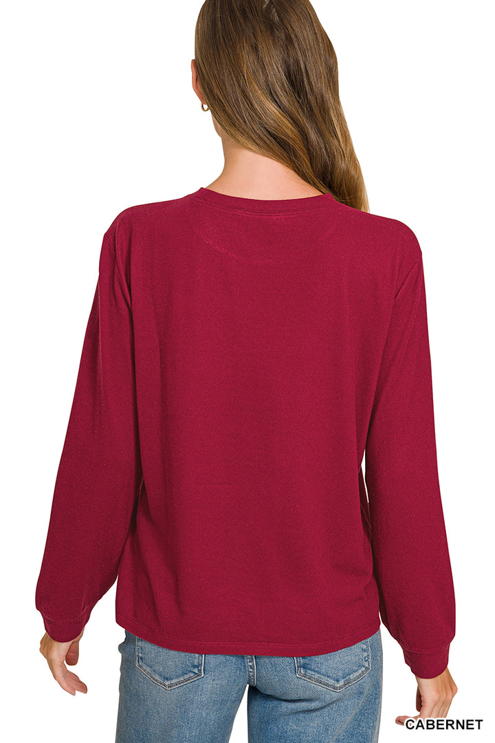 A woman shown from the back wearing a long-sleeve crewneck top in a deep burgundy or cabernet red color, paired with blue jeans, against a plain white background.
