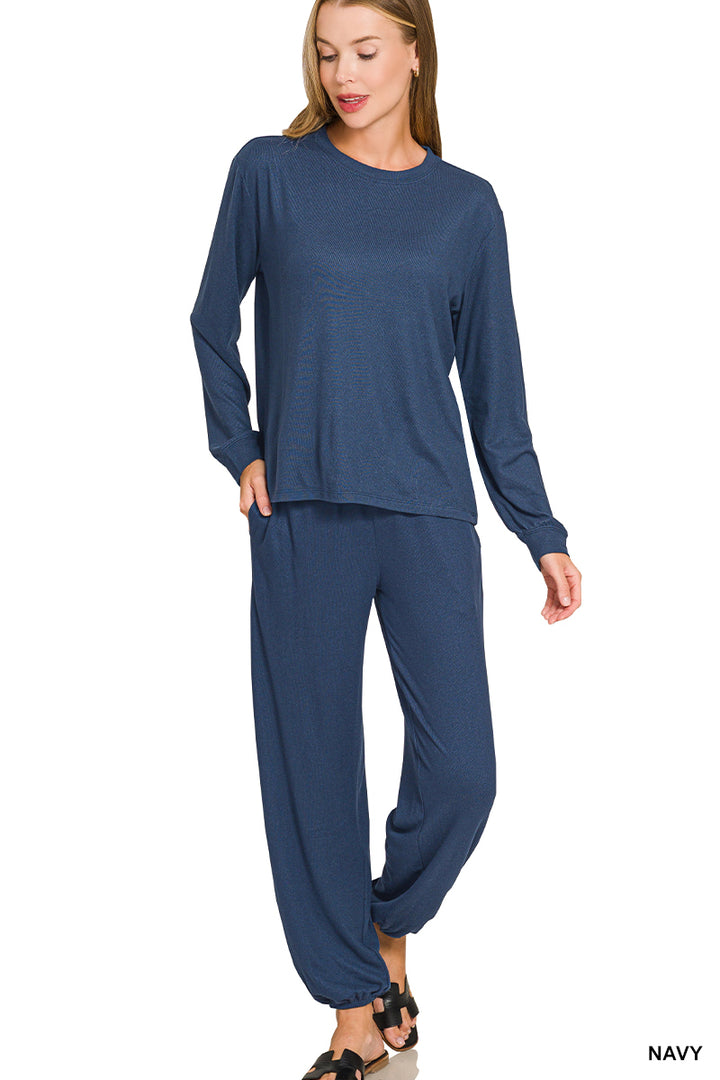 A woman modeling a matching navy blue lounge set consisting of a long-sleeve top and relaxed pants, shown against a plain white background.