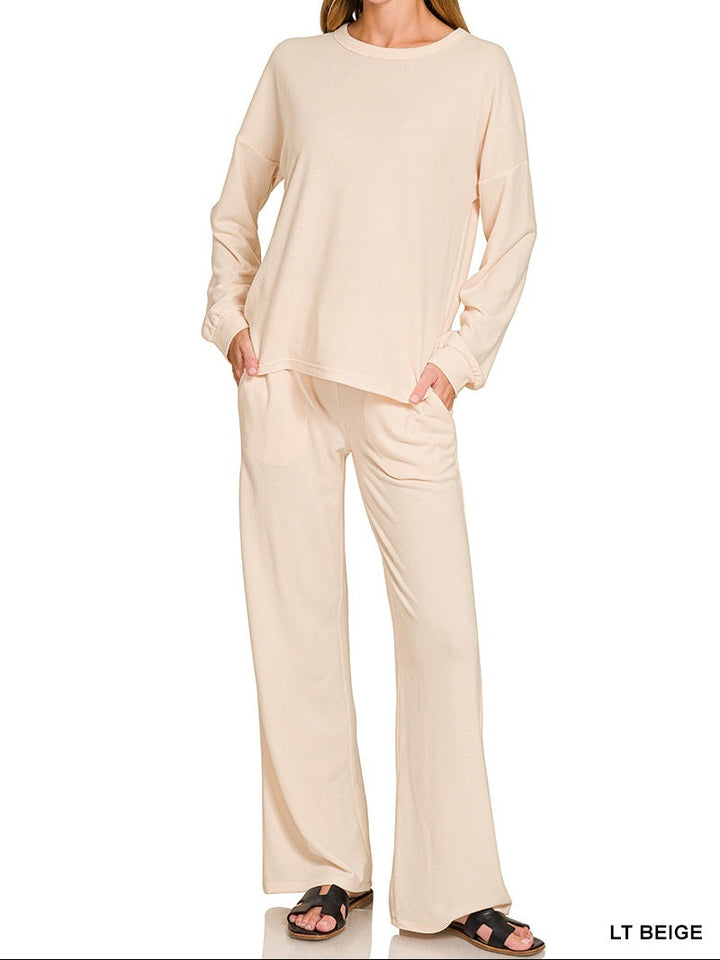 A woman modeling a light beige two-piece loungewear set consisting of a long-sleeve crewneck top and matching wide-leg pants, shown against a plain white background with text overlays indicating &