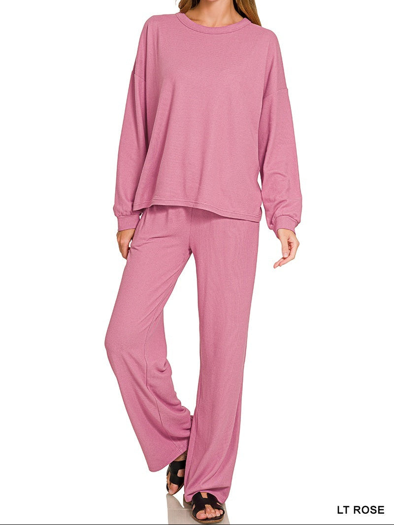 A woman modeling a matching dusty rose lounge set consisting of a long-sleeve cropped top and wide-leg pants, shown against a plain white background with &