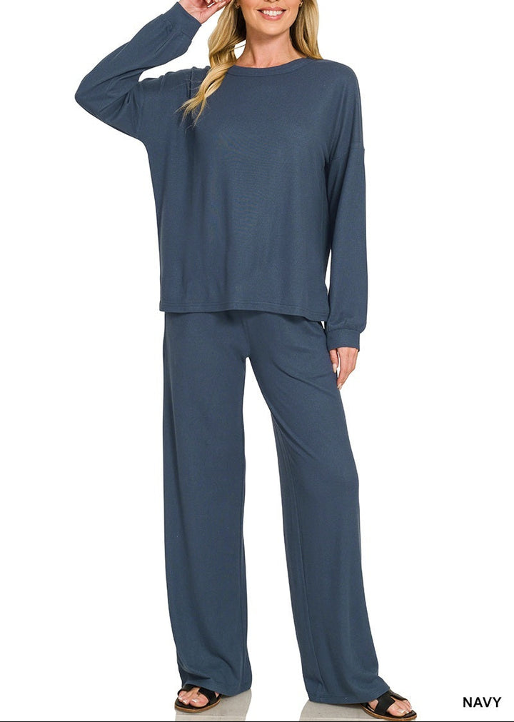 A woman modeling a matching navy blue loungewear set consisting of a long-sleeve top and wide-leg pants, shown against a plain white background with &