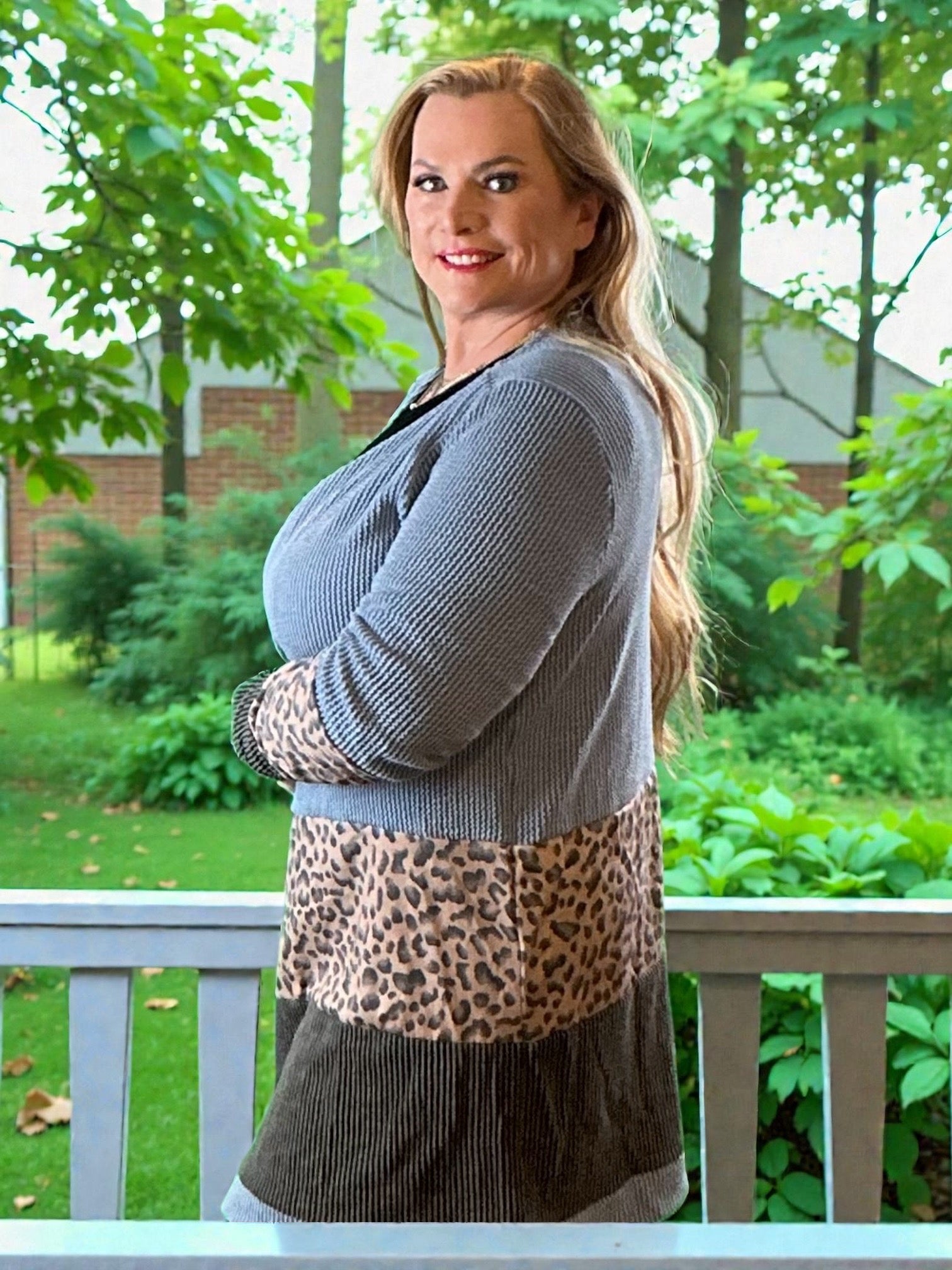 Woman wearing a layered outfit with a gray sweater, leopard print top, and dark skirt on a porch.