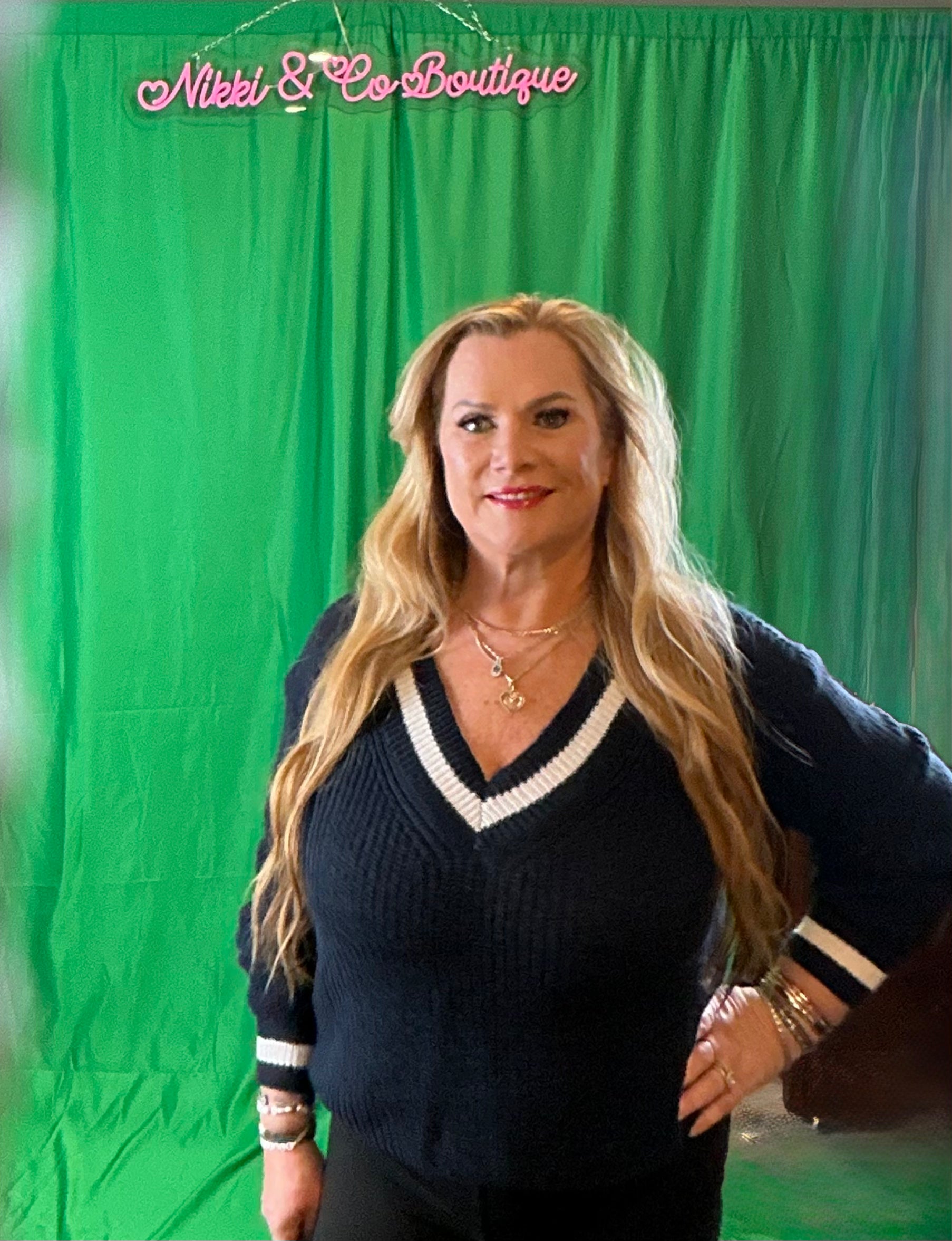 Woman posing in front of a green screen with 'Nikki & Co Boutique' branding.