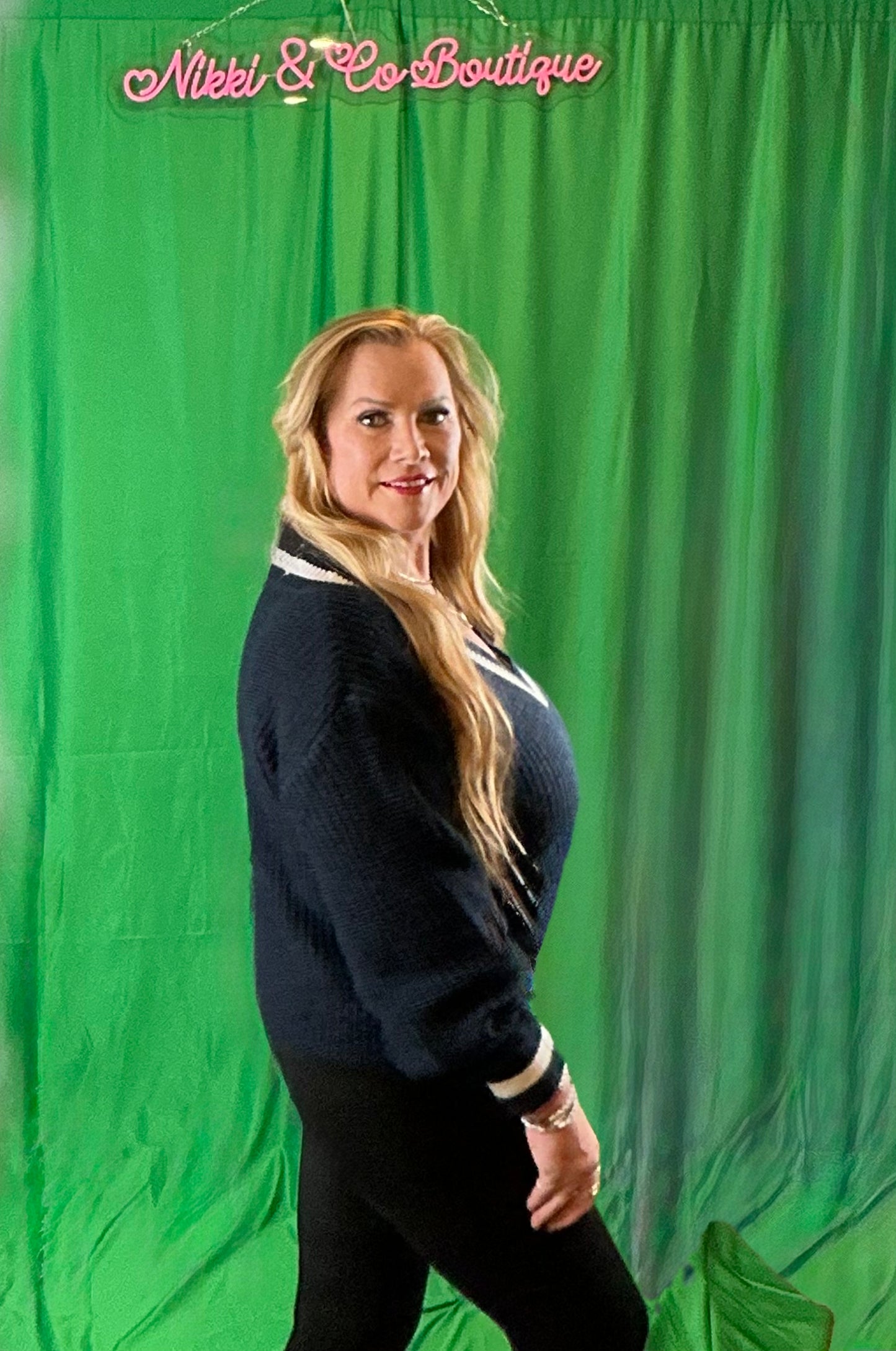 Woman posing in front of a green screen with 'Nikki & Co Boutique' branding.
