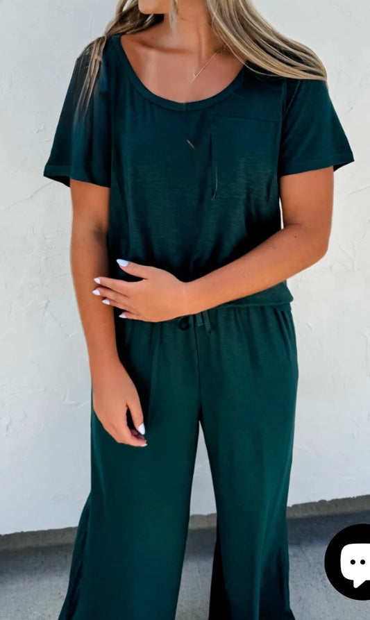 Person wearing a dark green outfit against a white wall