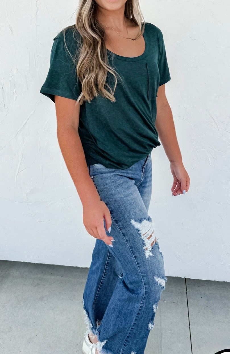 Person wearing a green t-shirt and ripped blue jeans against a white background