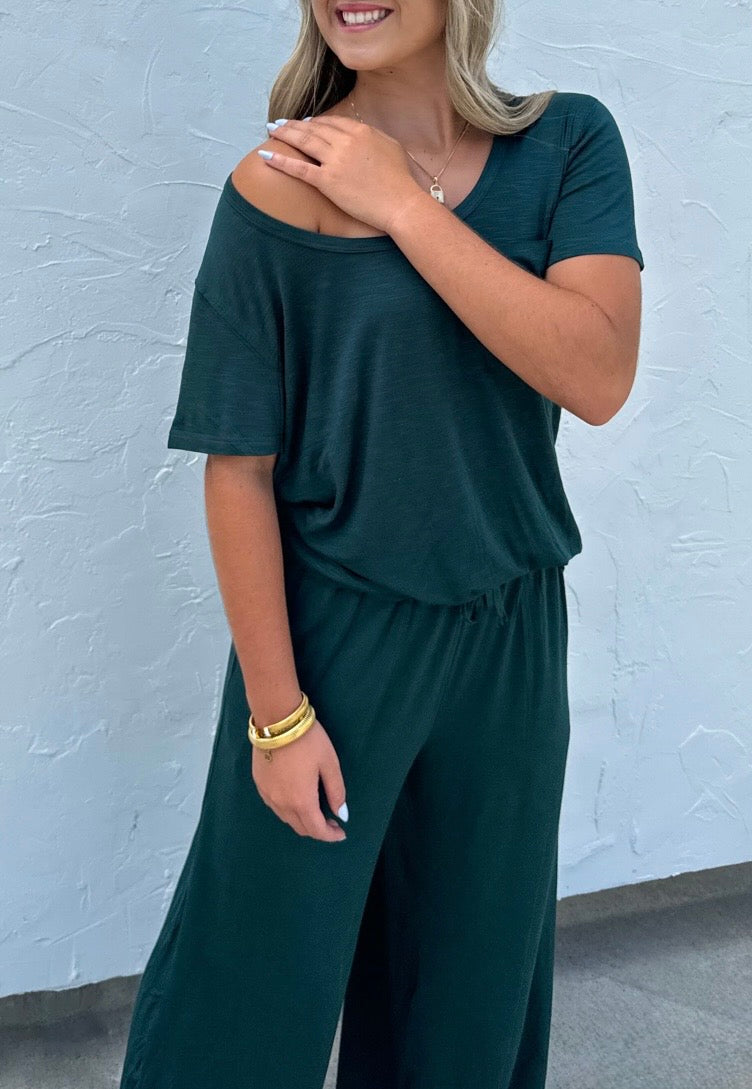 Woman wearing a dark green outfit against a light blue wall.
