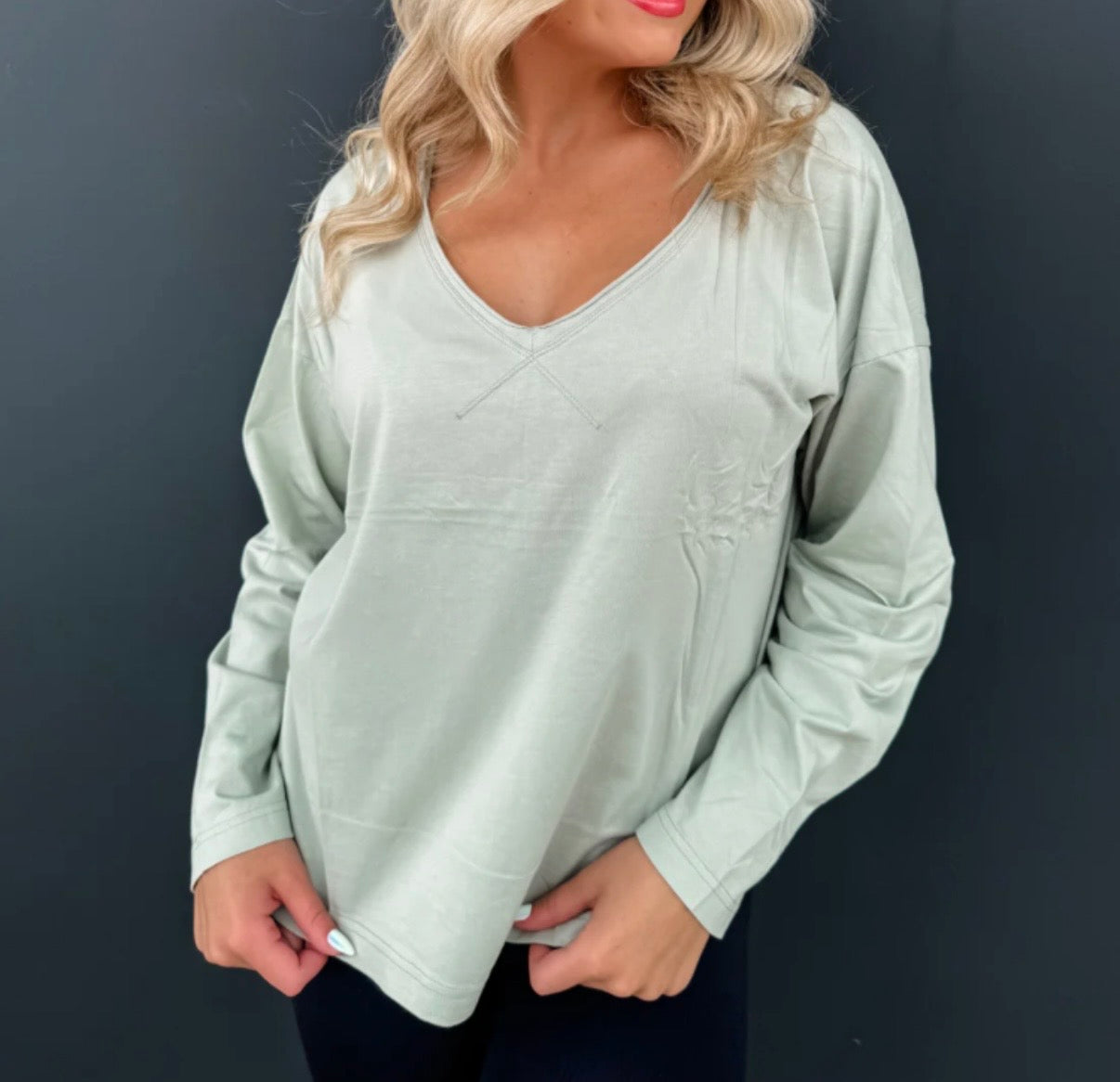 Woman wearing a light green long-sleeve top against a dark background