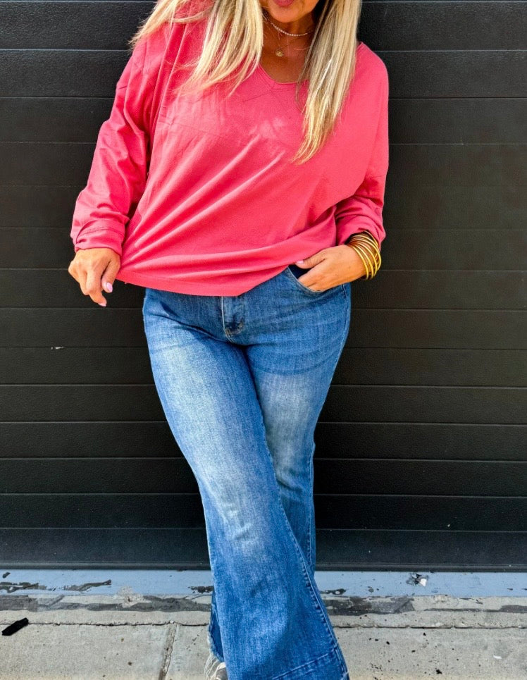 Person wearing a pink sweatshirt and blue jeans against a black wooden panel background