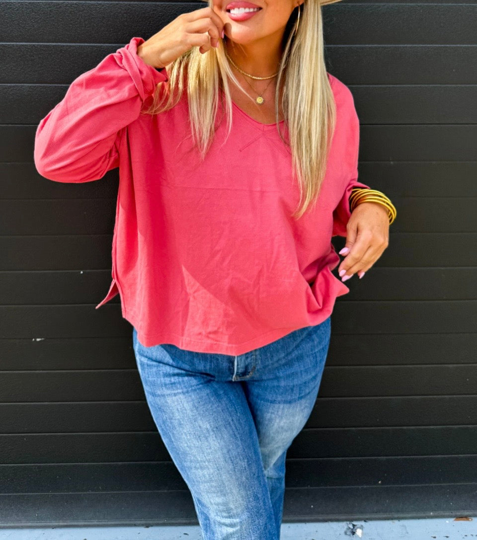 Woman wearing a pink long-sleeve top and blue jeans against a black background