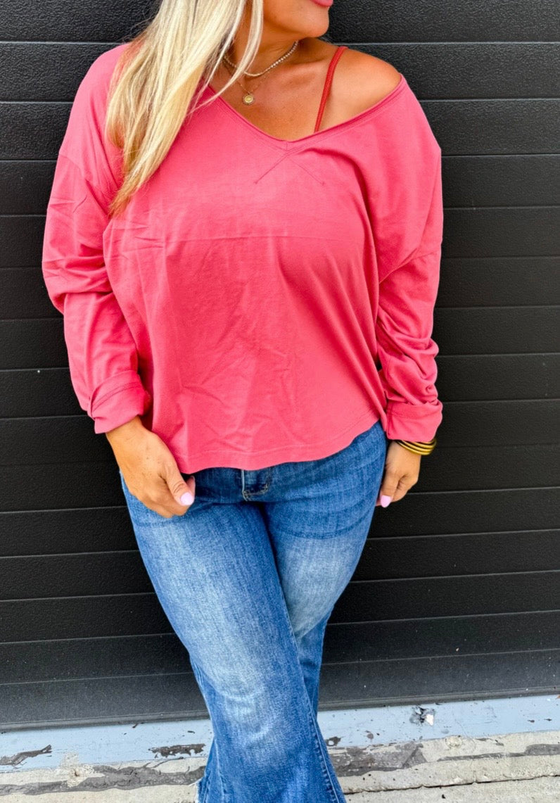 Person wearing a pink long-sleeve top and blue jeans against a black wall.
