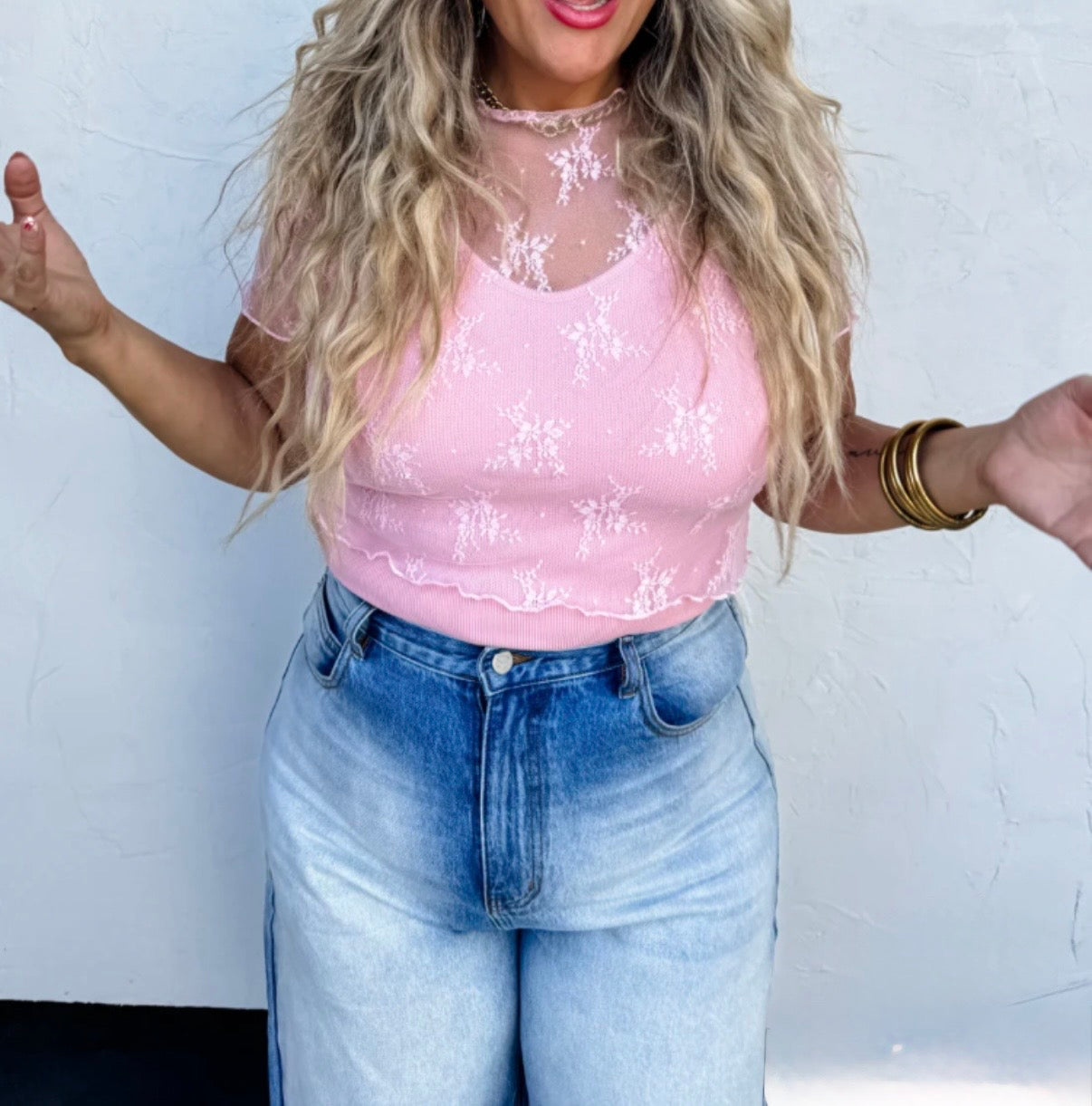Woman wearing a pink lace top and blue jeans against a white background