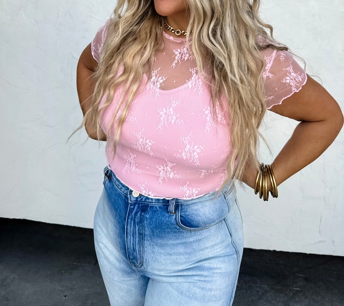 Woman wearing a pink lace top and blue jeans against a white background