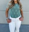 Person wearing a green lace top and white pants against a neutral background