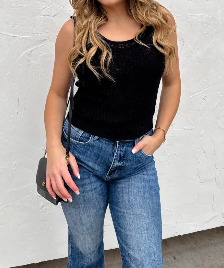 Person wearing a black tank top and blue jeans against a white wall.