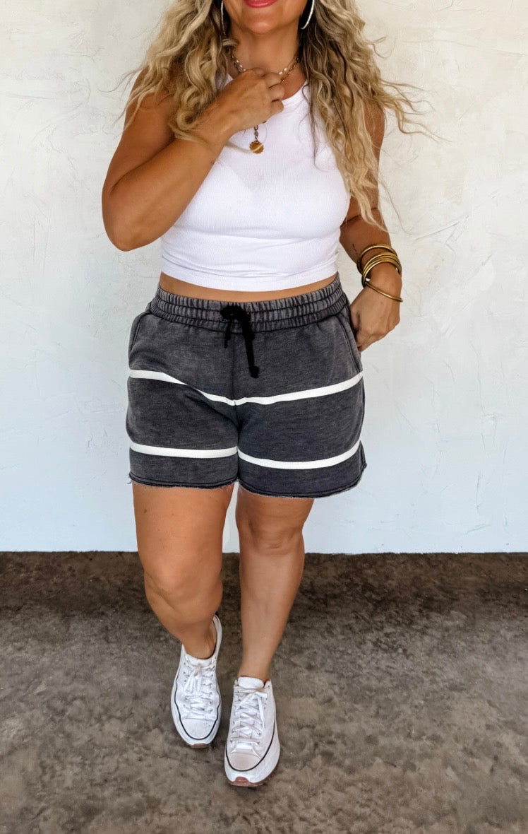 Woman wearing a white crop top and gray shorts with white stripes against a white background