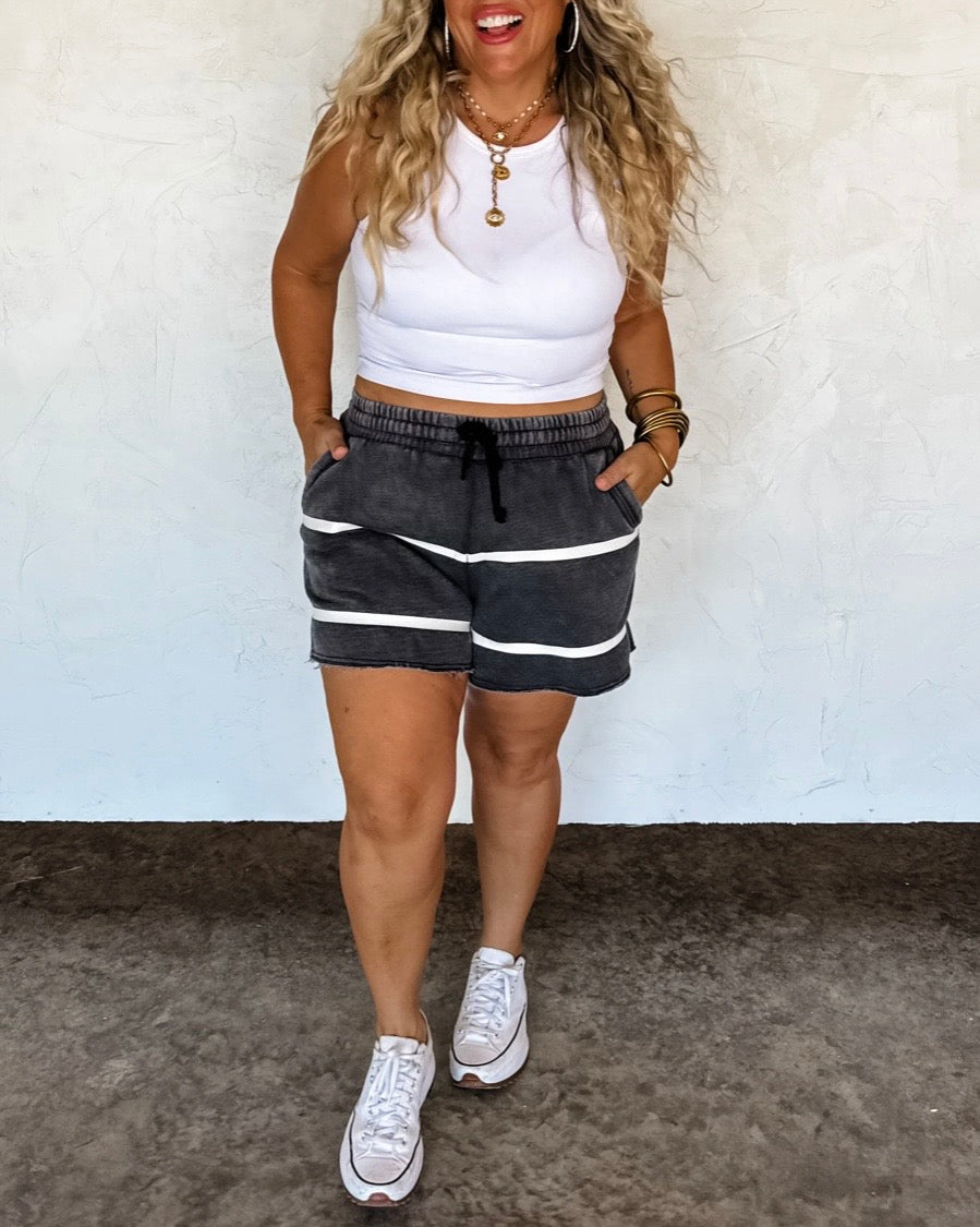 Woman wearing a white crop top and black shorts with white stripes against a plain background