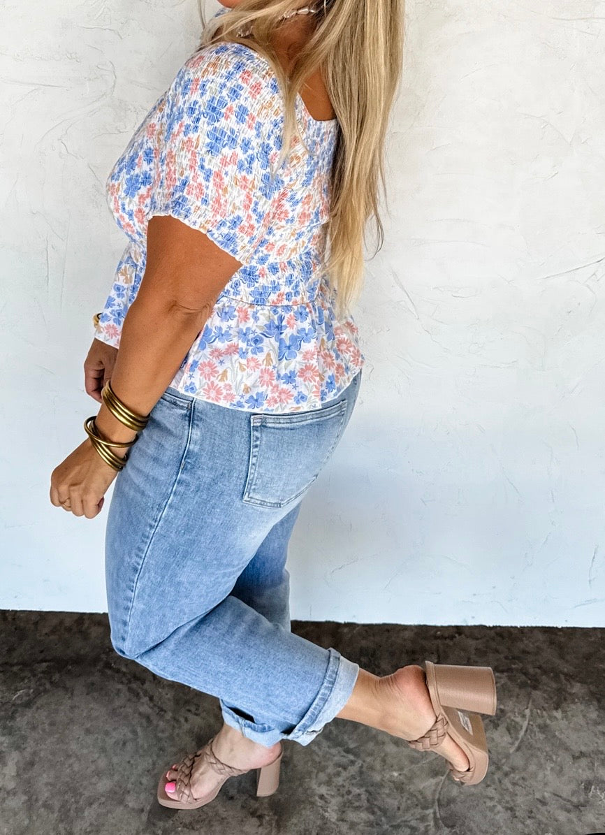 Woman wearing a floral blouse and jeans against a white wall