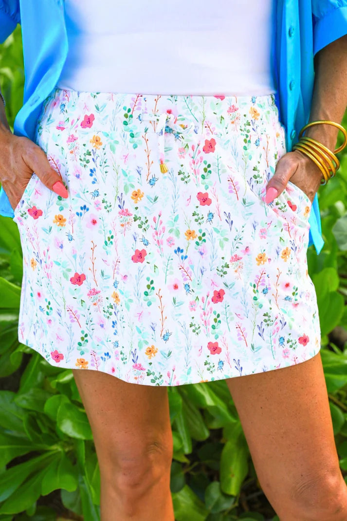 Person wearing a colorful floral skort with a blue top against a green leafy background