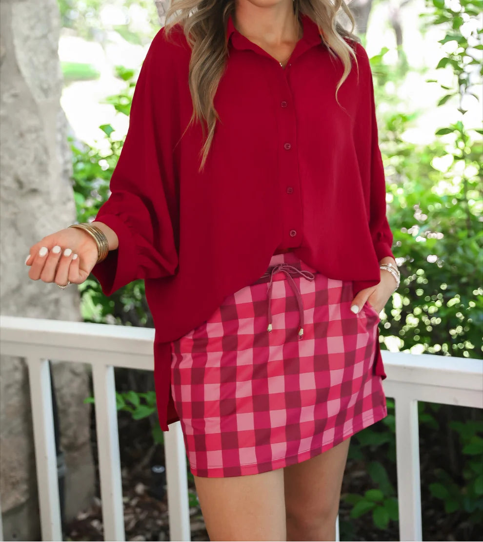 Woman wearing a red blouse and cranberry checkered skort outdoors.