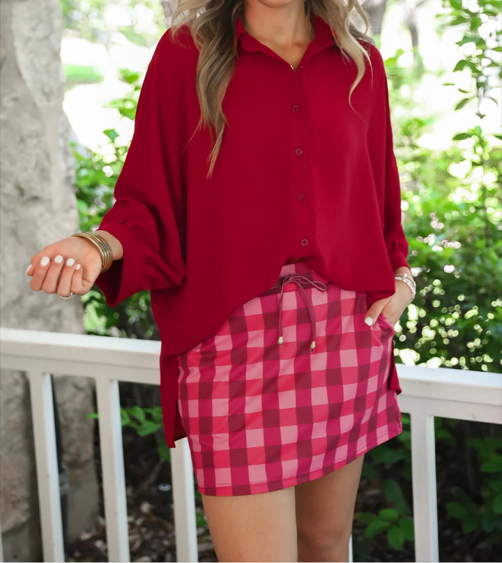 Woman wearing a red blouse and cranberry checkered skort outdoors.