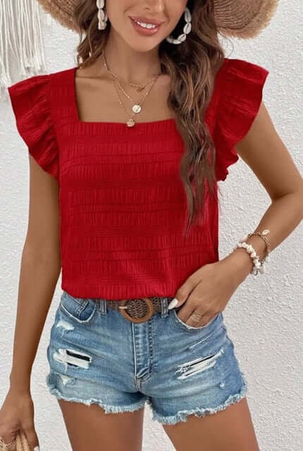 Woman wearing a red top with ruffled sleeves and denim shorts against a white background