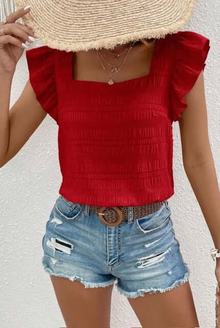 Person wearing a red top with ruffled sleeves and denim shorts on a white background