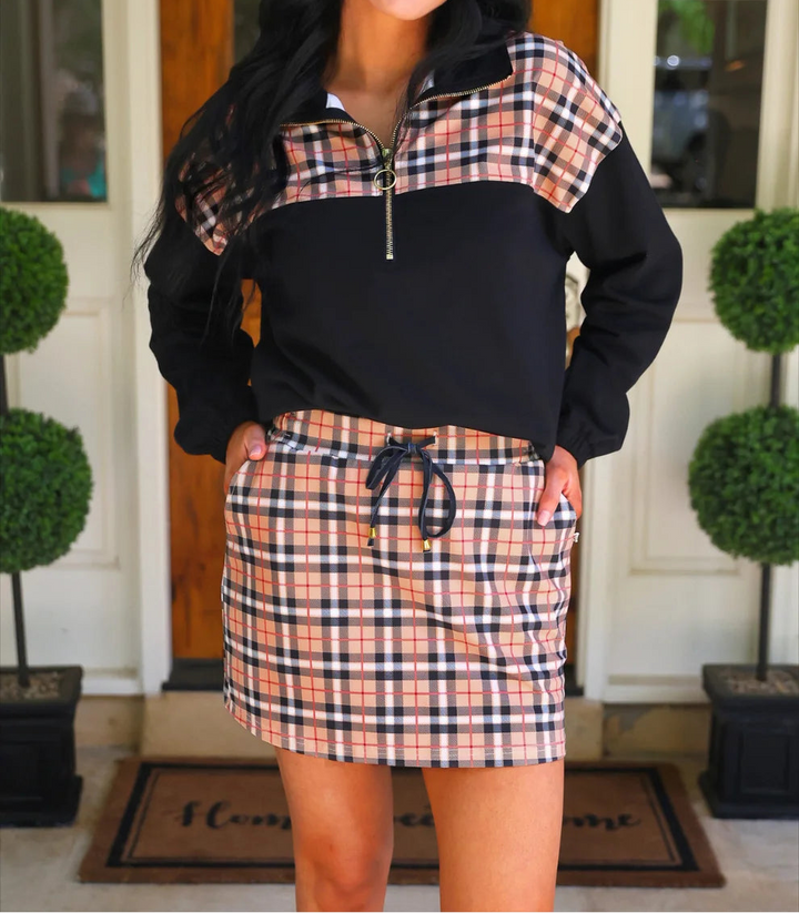 Woman wearing a plaid outfit with a black top and orange skirt in front of a wooden door.