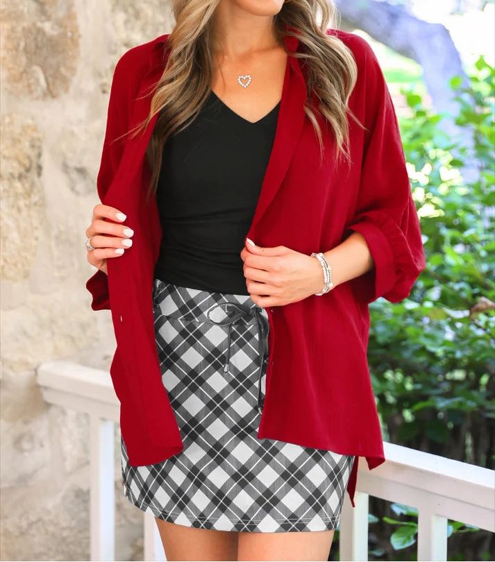 Woman wearing a black, v neck tee and black and white plaid skort with a red open blouse.