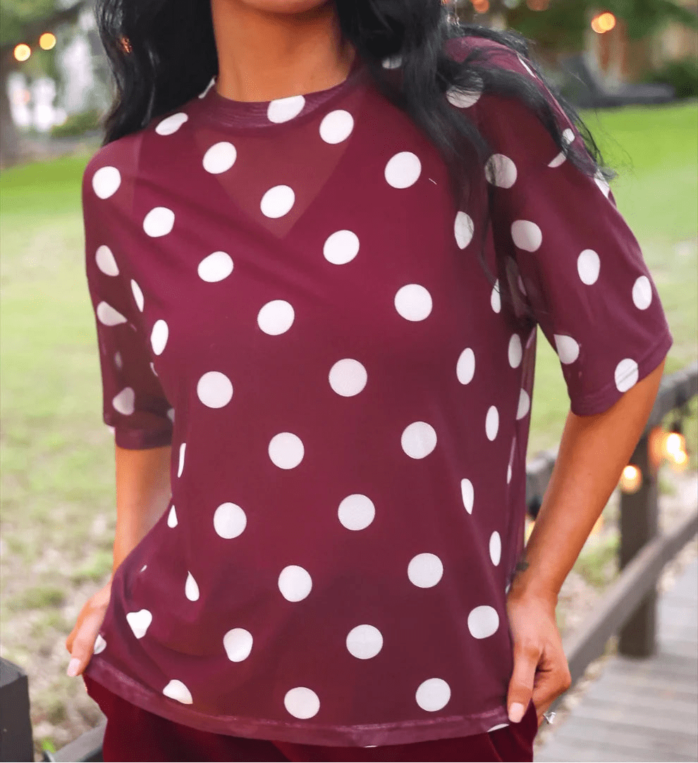 Woman wearing a maroon top with white polka dots outdoors.