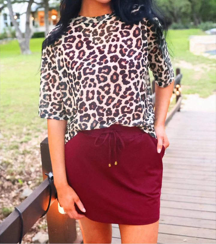 Woman wearing a leopard print top and burgundy skort outdoors.